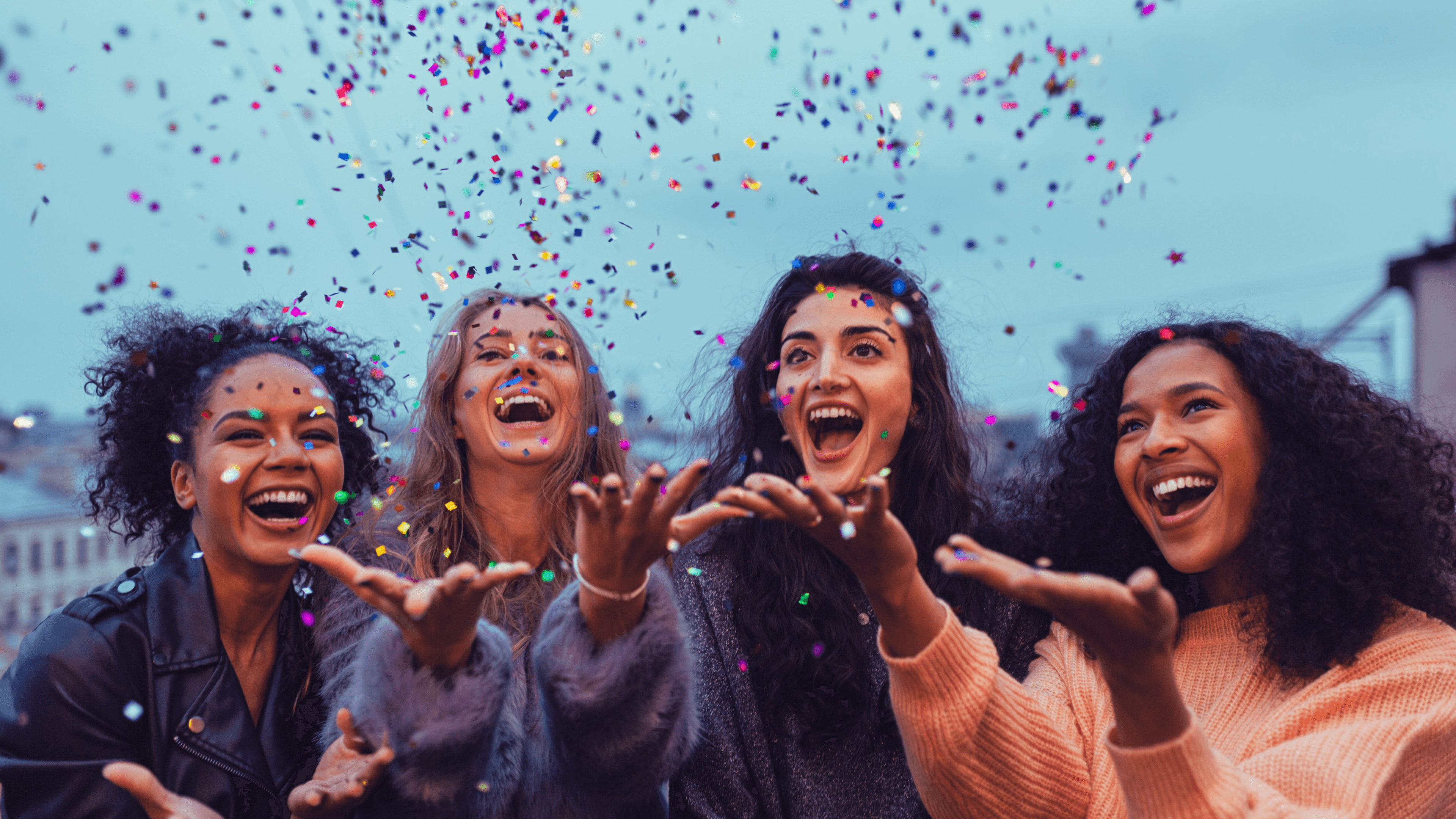 Bunt gemischte Gruppe junger Frauen, die Konfetti in die Luft werfen, gemeinsam feiern und sich freuen.